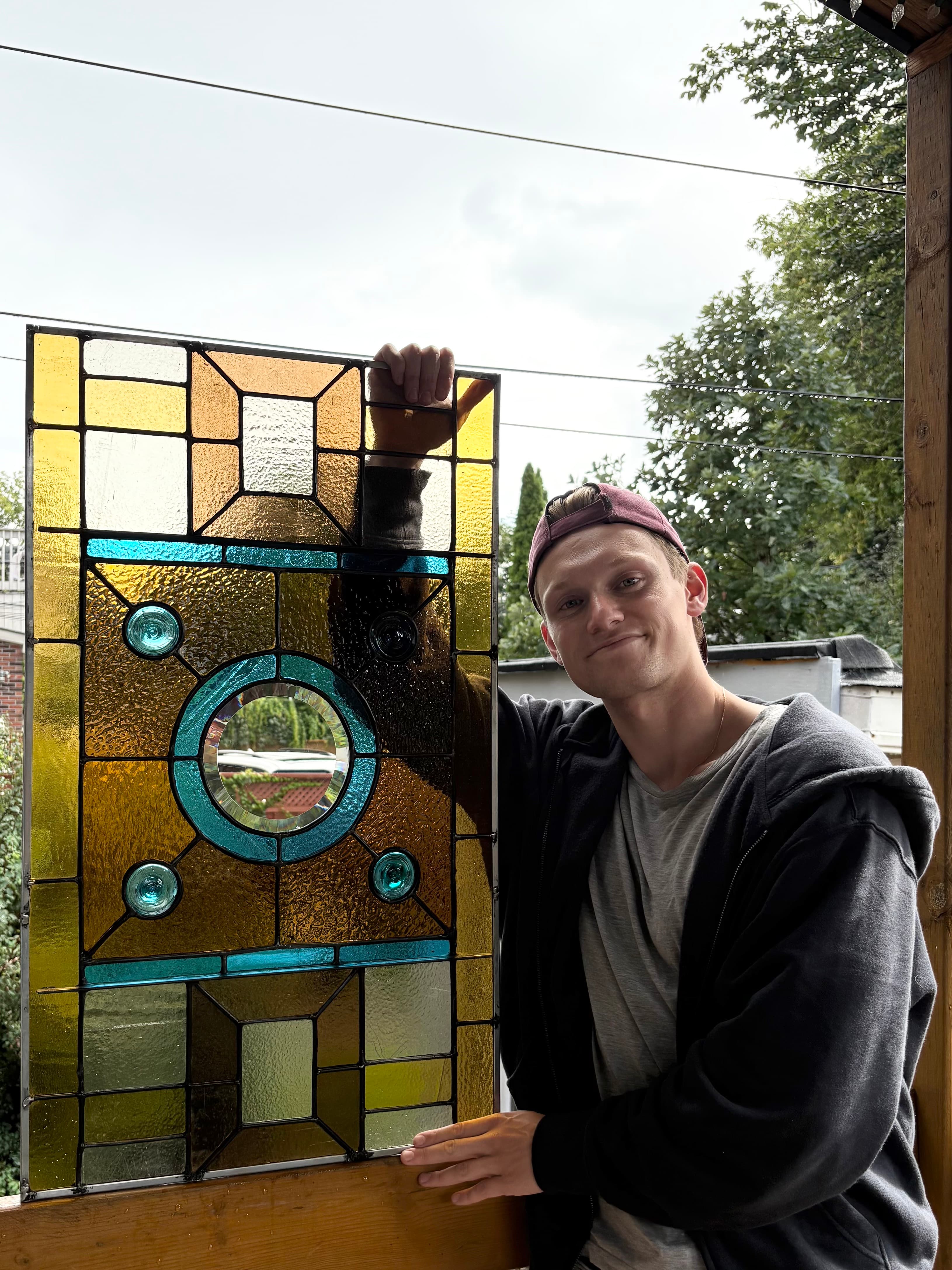 Dylan Ford, stained glass artist and founder of Sunday Projects, holding a custom leaded glass window in Toronto